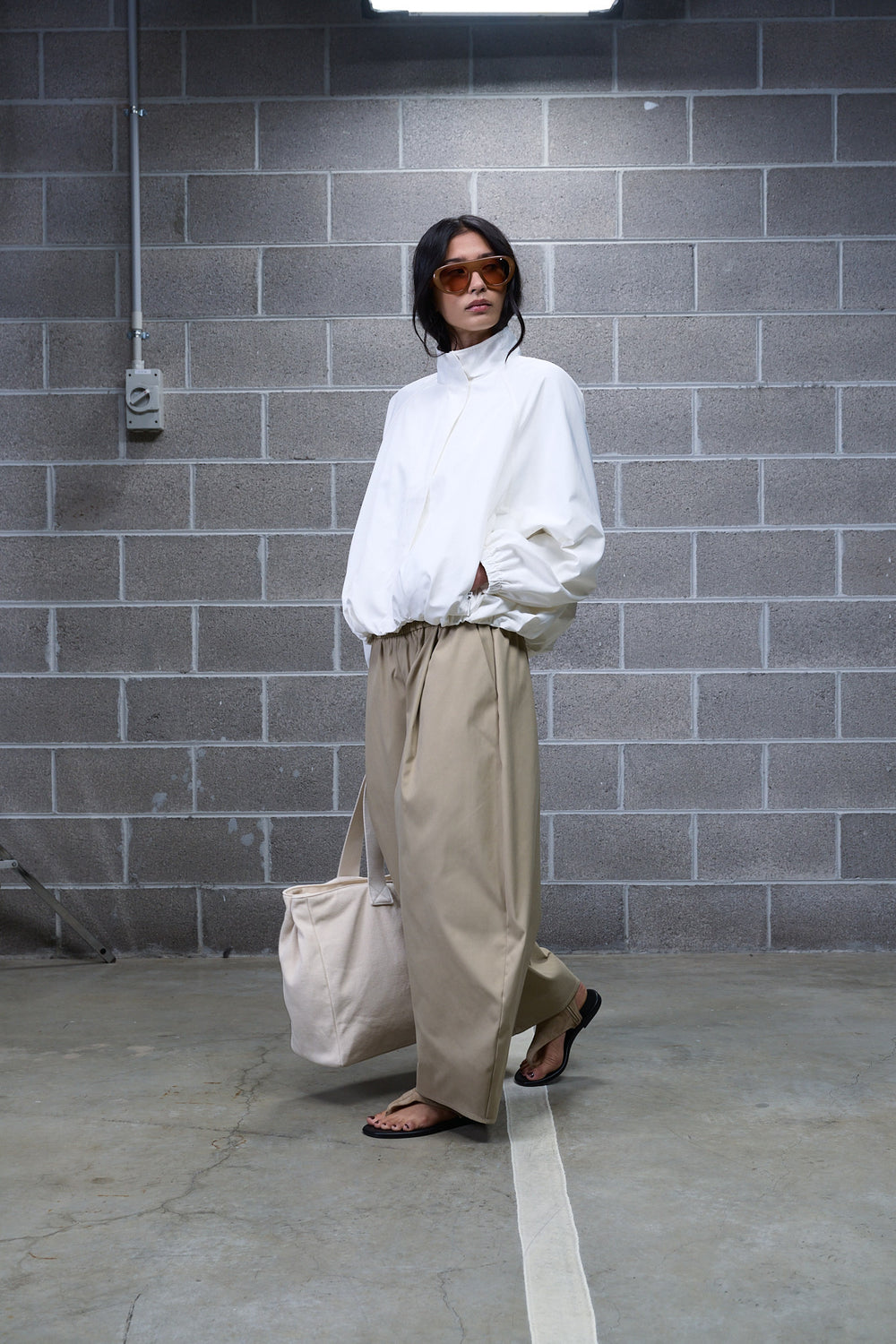 Woman wearing beige barrel leg pants with a white high neck blouse, tote bag and flat sandals
