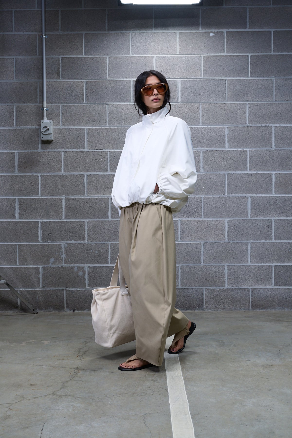 Woman wearing beige barrel leg pants with a white high neck blouse, tote bag and flat sandals