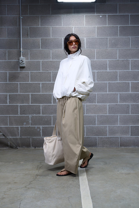 Woman wearing beige barrel leg pants with a white high neck blouse, tote bag and flat sandals