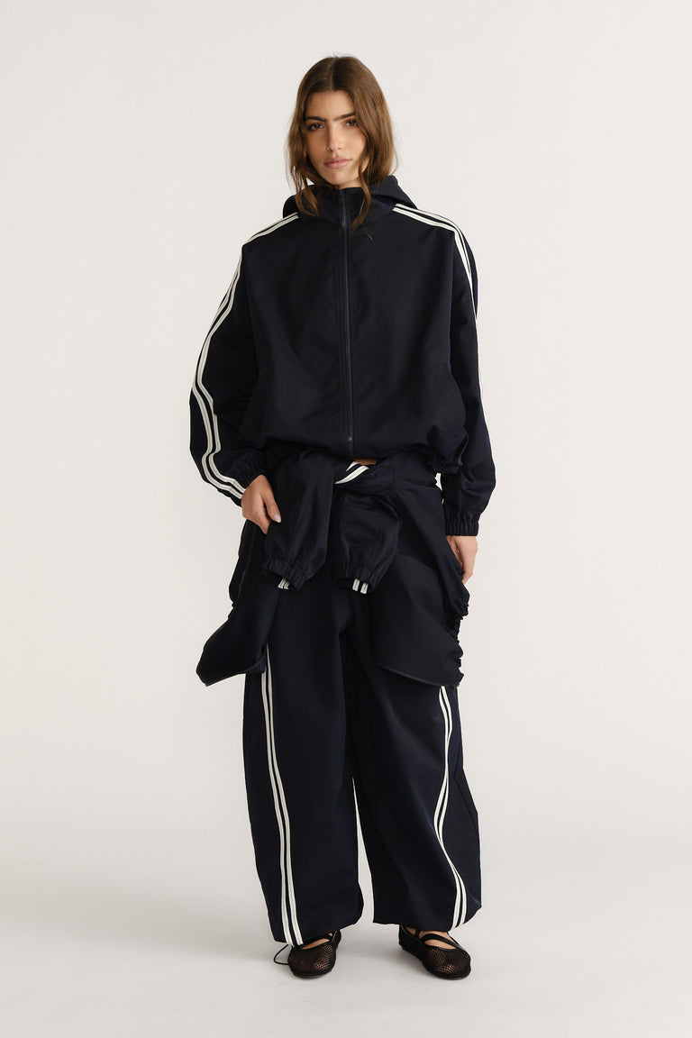 Woman wearing a relaxed navy hooded jacket and matching wide-leg pants with white stripes for a sporty, casual look