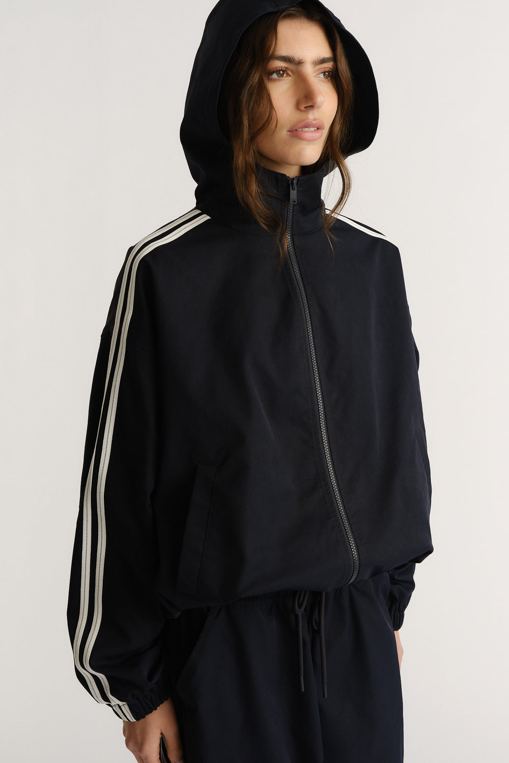 Woman wearing a navy hooded jacket with white side stripes and elasticated cuffs, styled for a laid-back sporty look