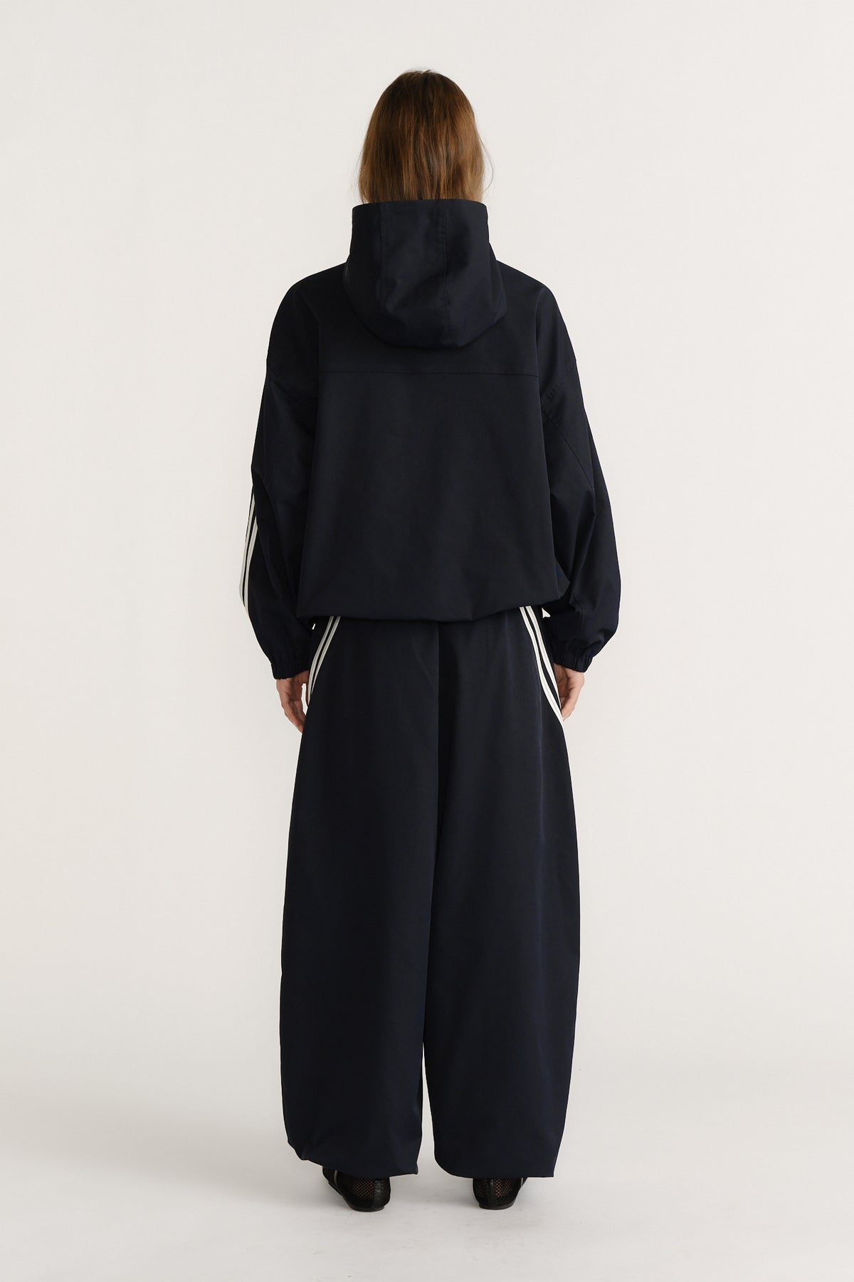 Woman seen from behind wearing a navy hooded jacket with white stripe details paired with wide-leg matching pants