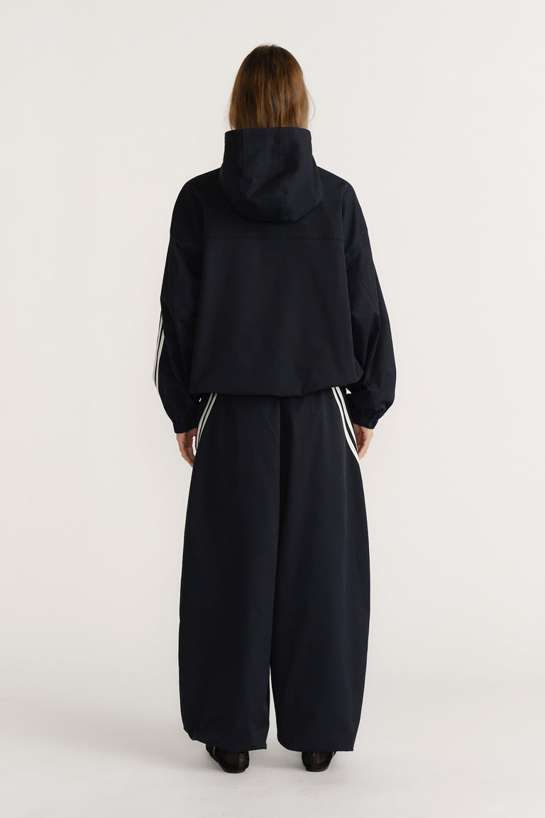 Woman seen from behind wearing a navy hooded jacket with white stripe details paired with wide-leg matching pants