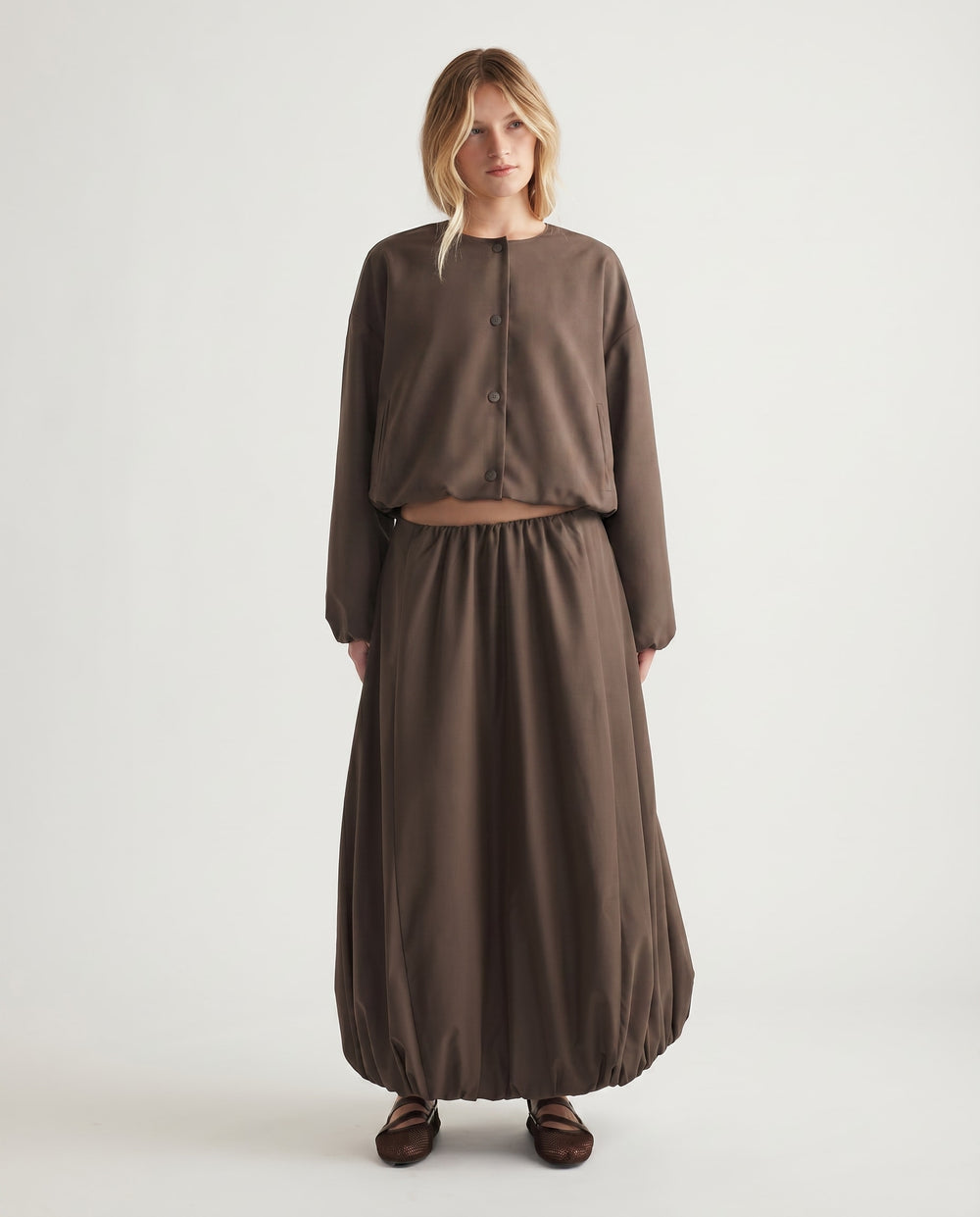 Woman wearing a relaxed-fit brown midi skirt with a bubble hem and matching long-sleeve buttoned top for effortless style.
