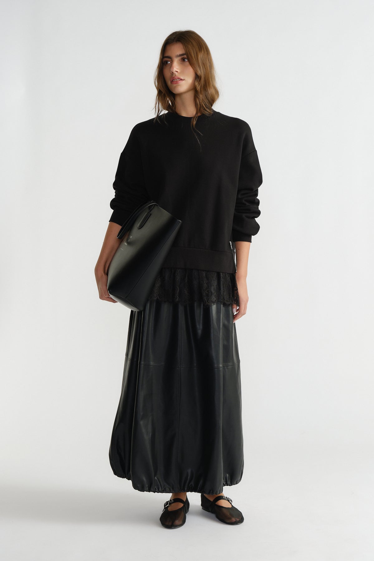 Woman wearing a black lace-trimmed sweatshirt paired with a long leather skirt and carrying a large black tote bag.