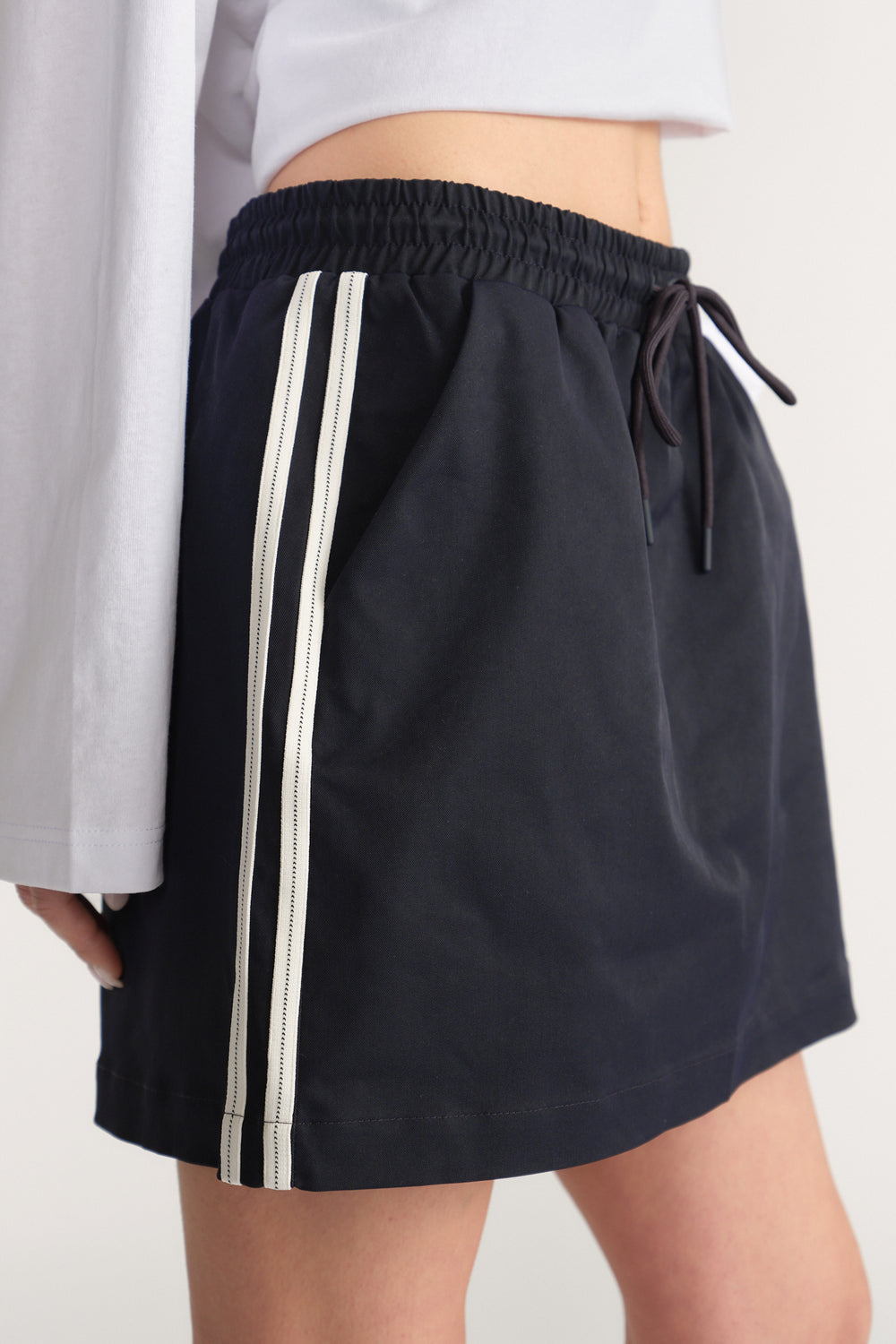 Woman wearing a black mini skirt with an elastic drawstring waist and white side stripe
