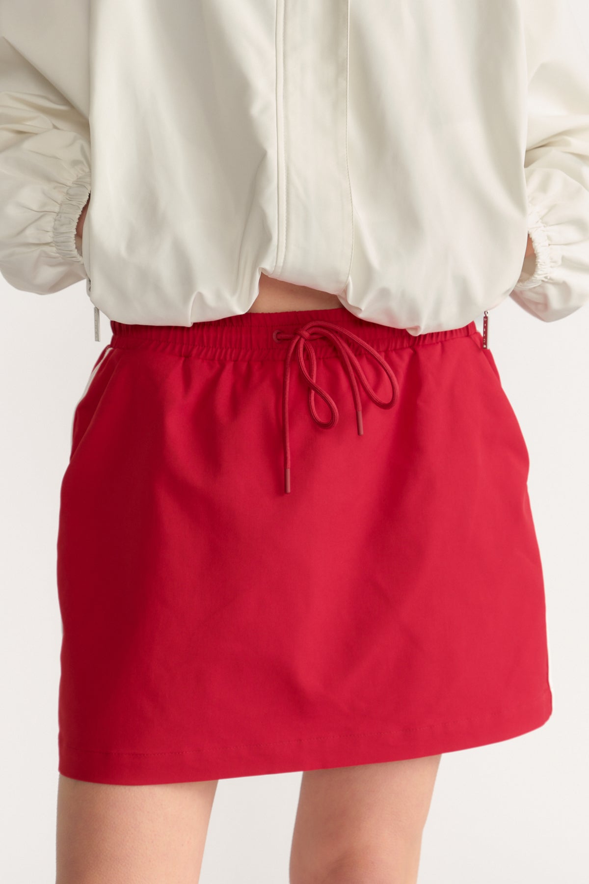 Model wearing a red elastic waist mini skirt with drawstring and a cropped white blouse