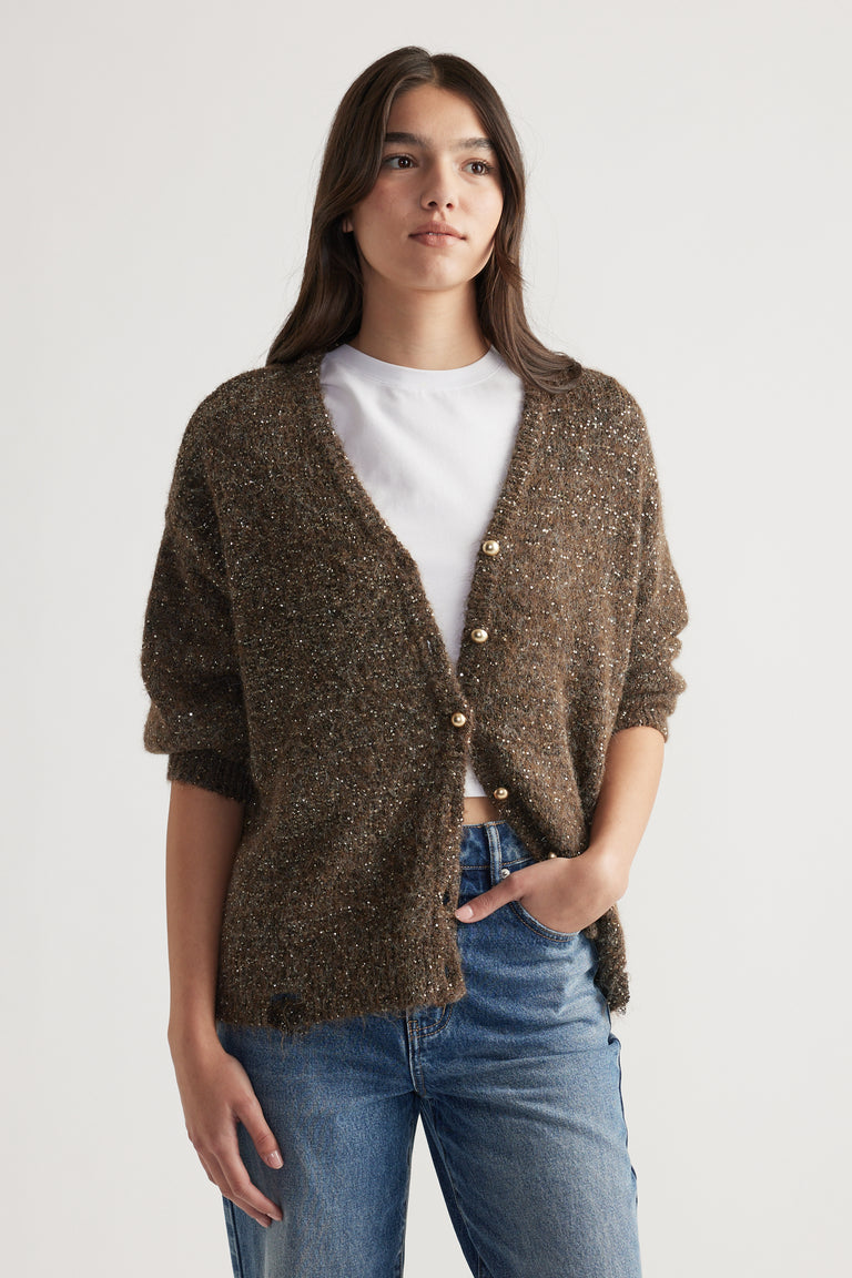 Woman wearing a relaxed fit dark bronze sequin cardigan with pearl buttons over a white top and blue jeans