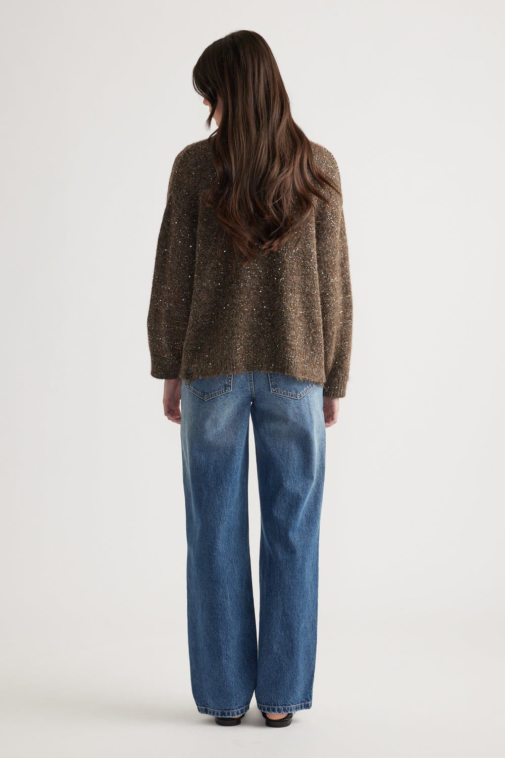Back view of a woman wearing a relaxed fit distressed sequin cardigan paired with classic blue straight-leg jeans