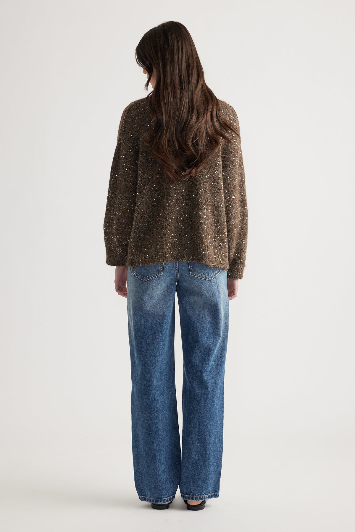 Back view of a woman wearing a relaxed fit distressed sequin cardigan paired with classic blue straight-leg jeans