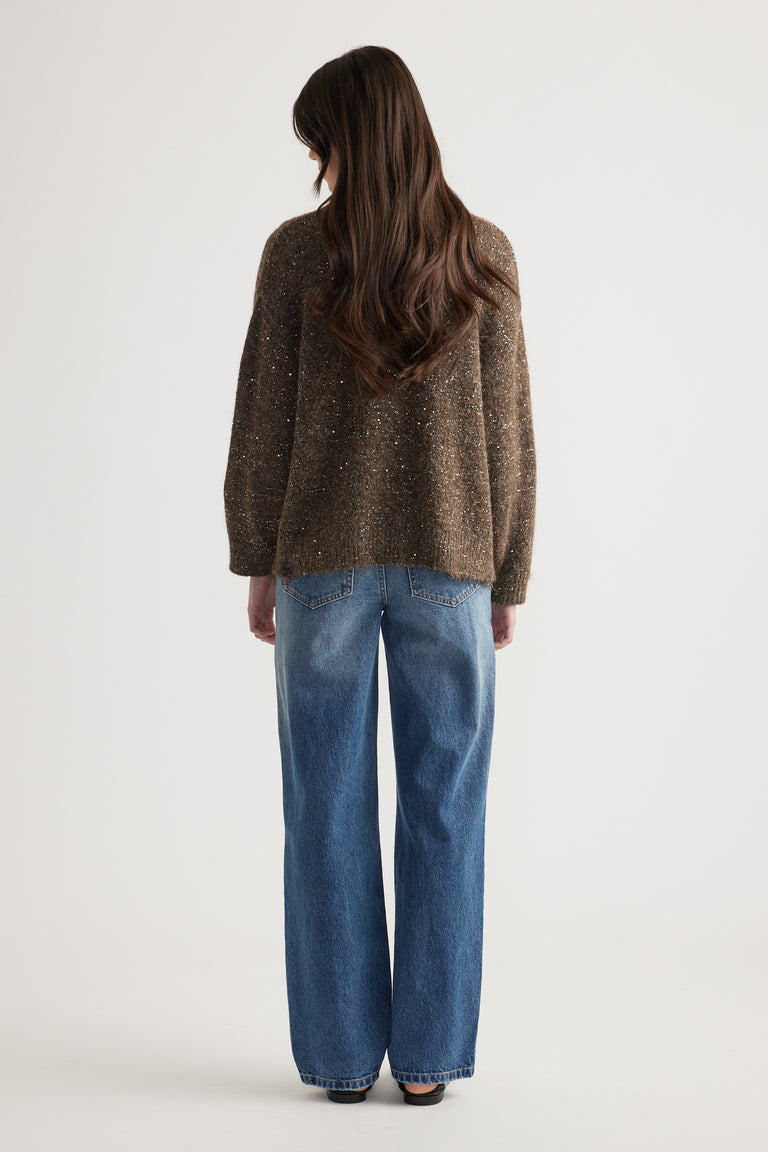 Back view of a woman wearing a relaxed fit distressed sequin cardigan paired with classic blue straight-leg jeans