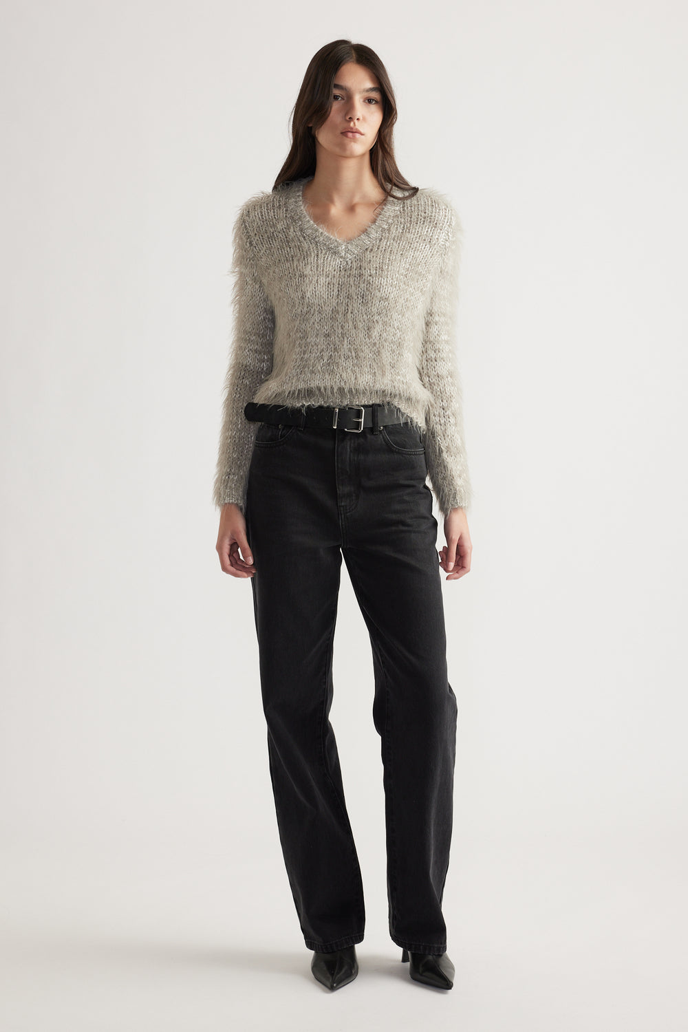 Woman standing wearing a soft textured V-neck knit jumper paired with high-waisted black jeans and pointed boots
