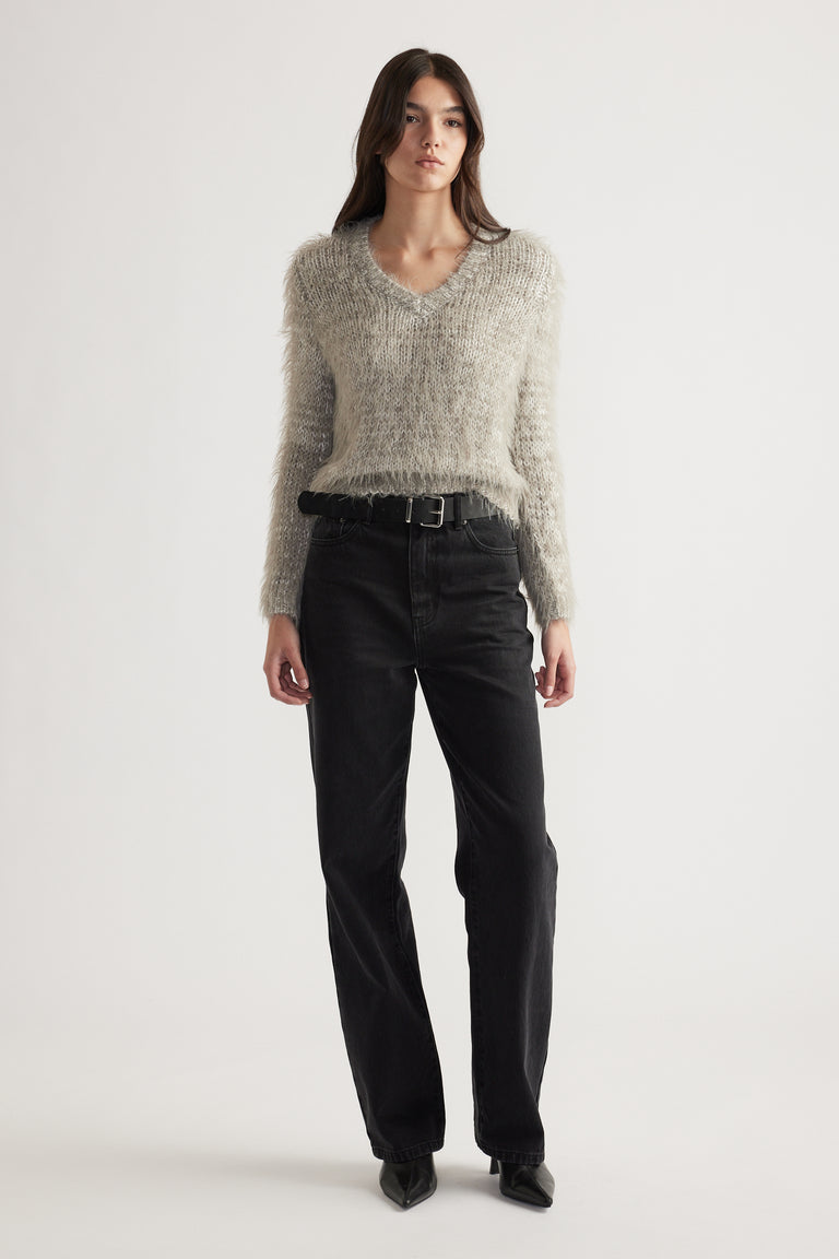 Woman standing wearing a soft textured V-neck knit jumper paired with high-waisted black jeans and pointed boots