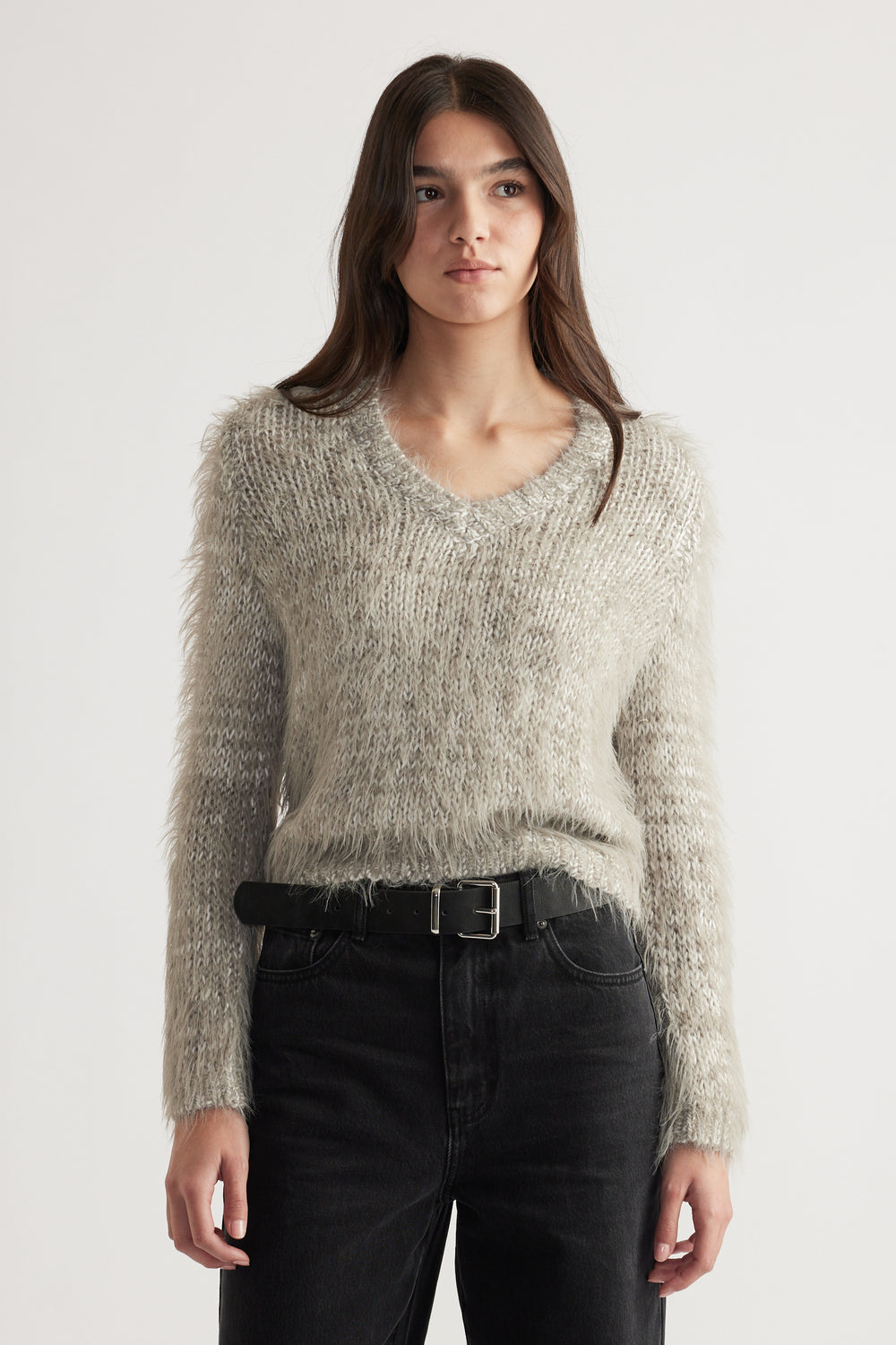 Woman wearing a soft textured grey V-neck jumper paired with black high-waisted jeans and a black belt