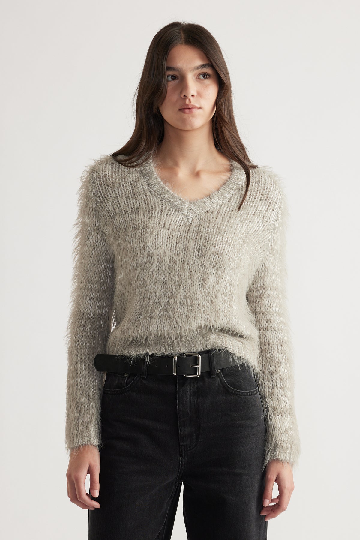 Woman wearing a soft textured grey V-neck jumper paired with black high-waisted jeans and a black belt