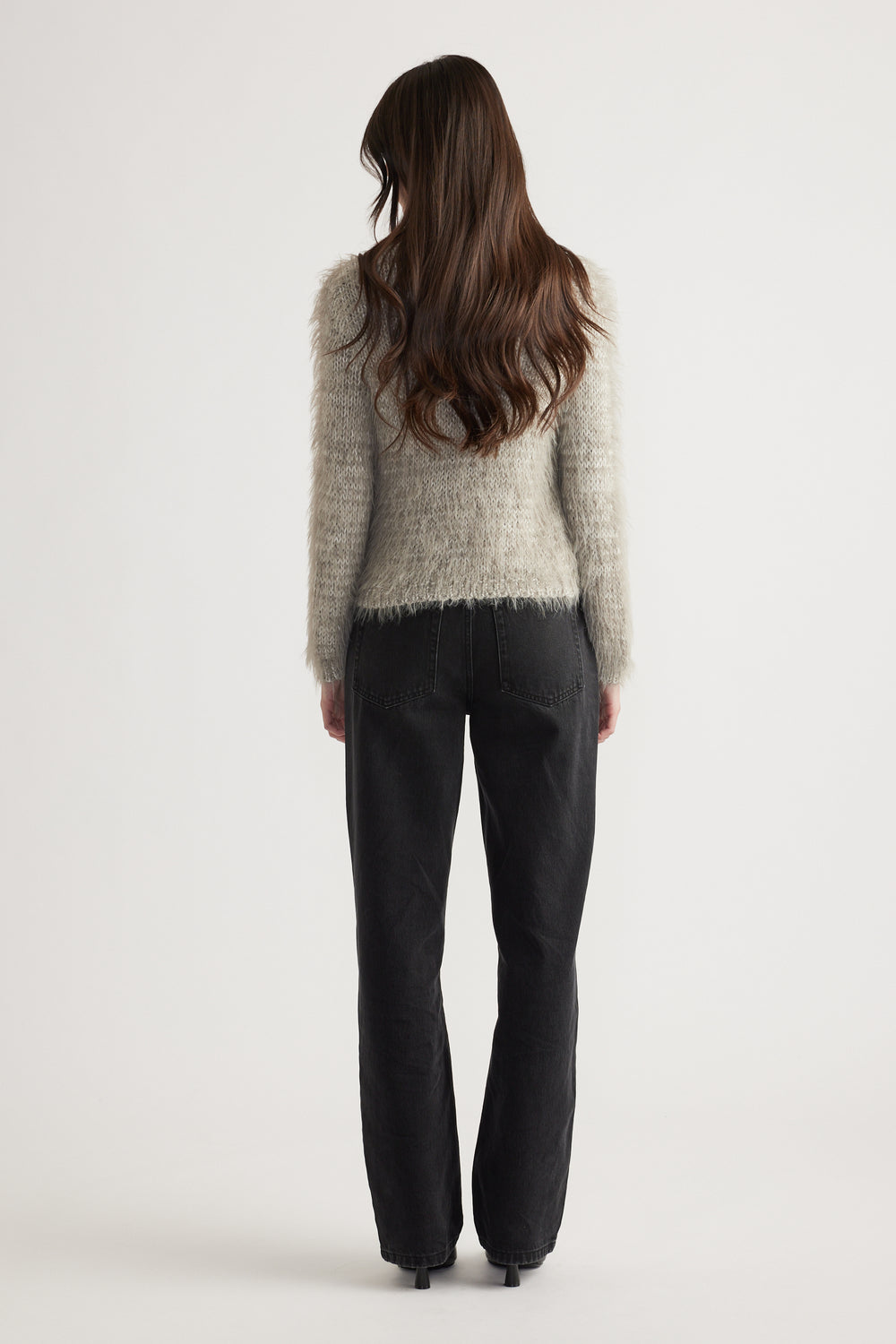 Woman seen from behind wearing a soft textured knit jumper in light grey paired with relaxed black jeans and heels