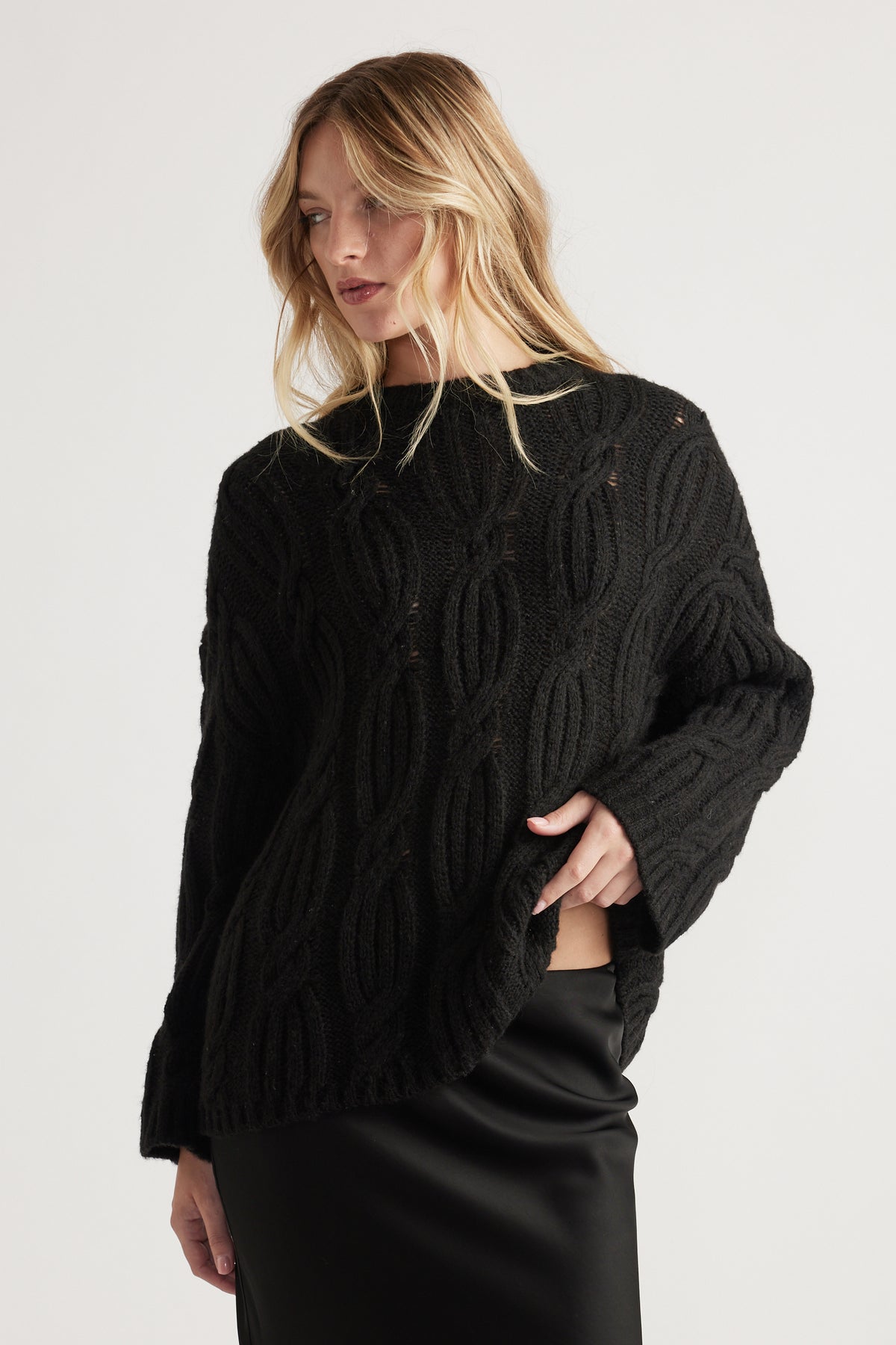 Woman wearing a black cable knit jumper with a cozy relaxed fit paired with a sleek black skirt for a casual chic look