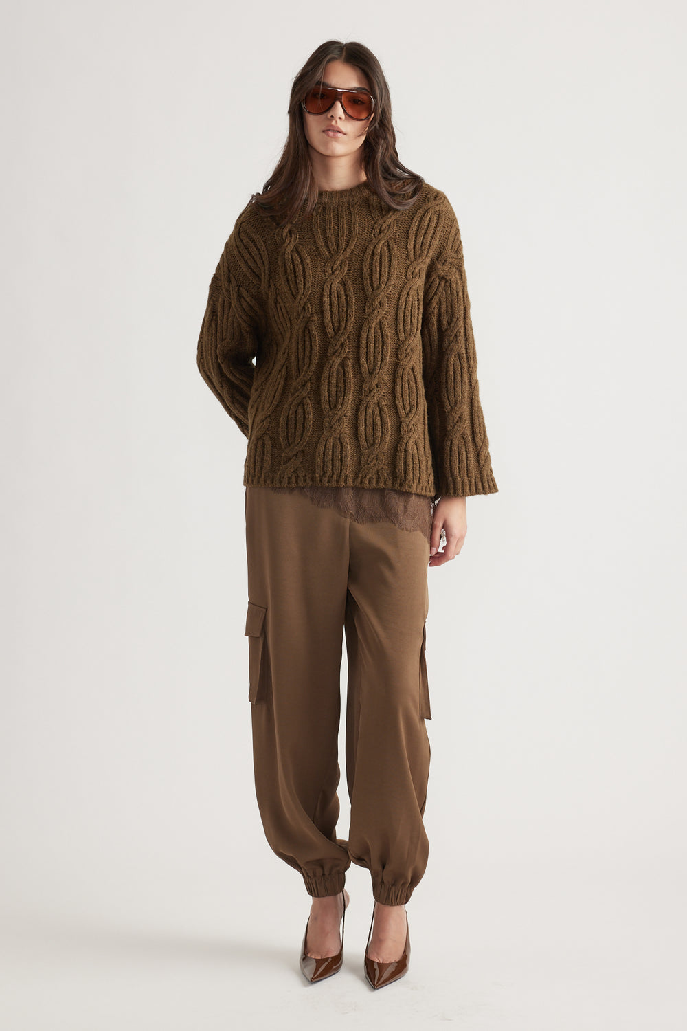 Woman wearing a textured cable knit jumper in bronze paired with relaxed cargo pants and brown pointed heels, styled with oversized sunglasses
