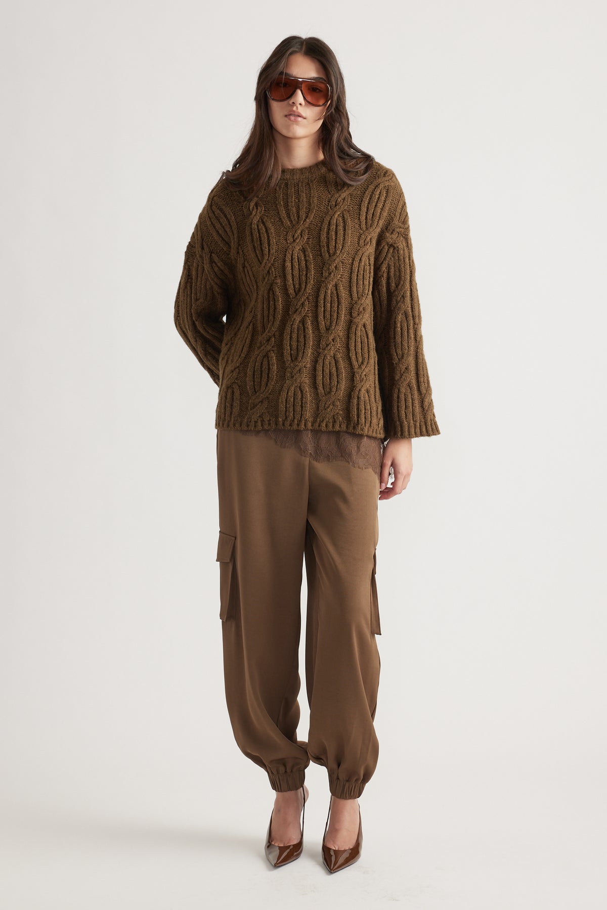 Woman wearing a textured cable knit jumper in bronze paired with relaxed cargo pants and brown pointed heels, styled with oversized sunglasses