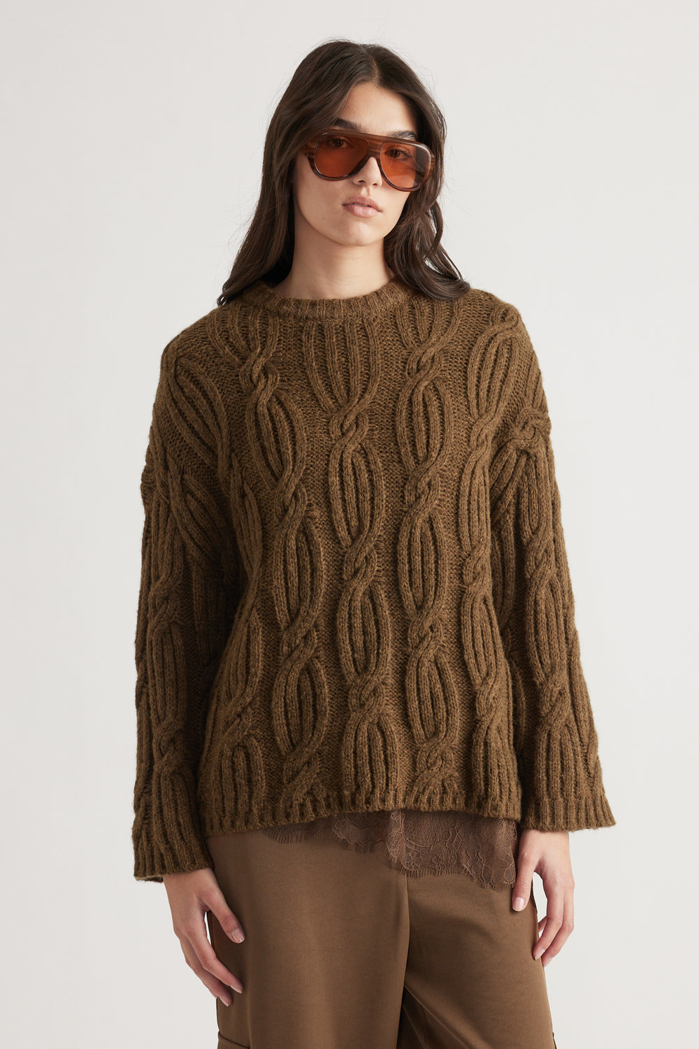 Woman wearing a chunky brown cable knit jumper paired with loose brown pants and oversized amber sunglasses