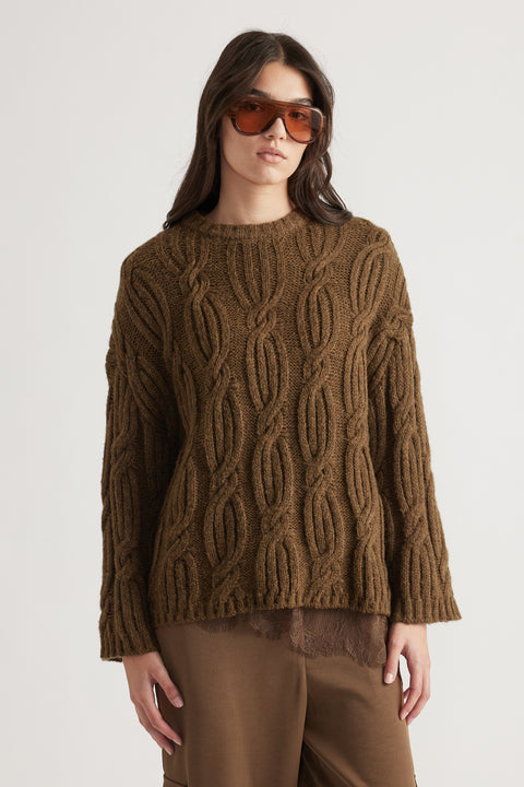 Woman wearing a chunky brown cable knit jumper paired with loose brown pants and oversized amber sunglasses