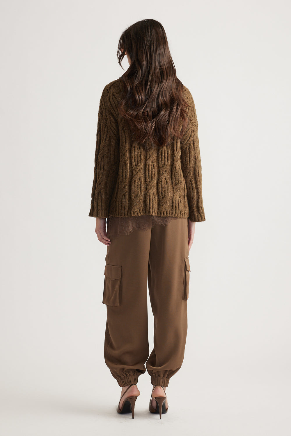 Woman seen from behind wearing a textured brown cable knit jumper paired with relaxed cargo pants and heels
