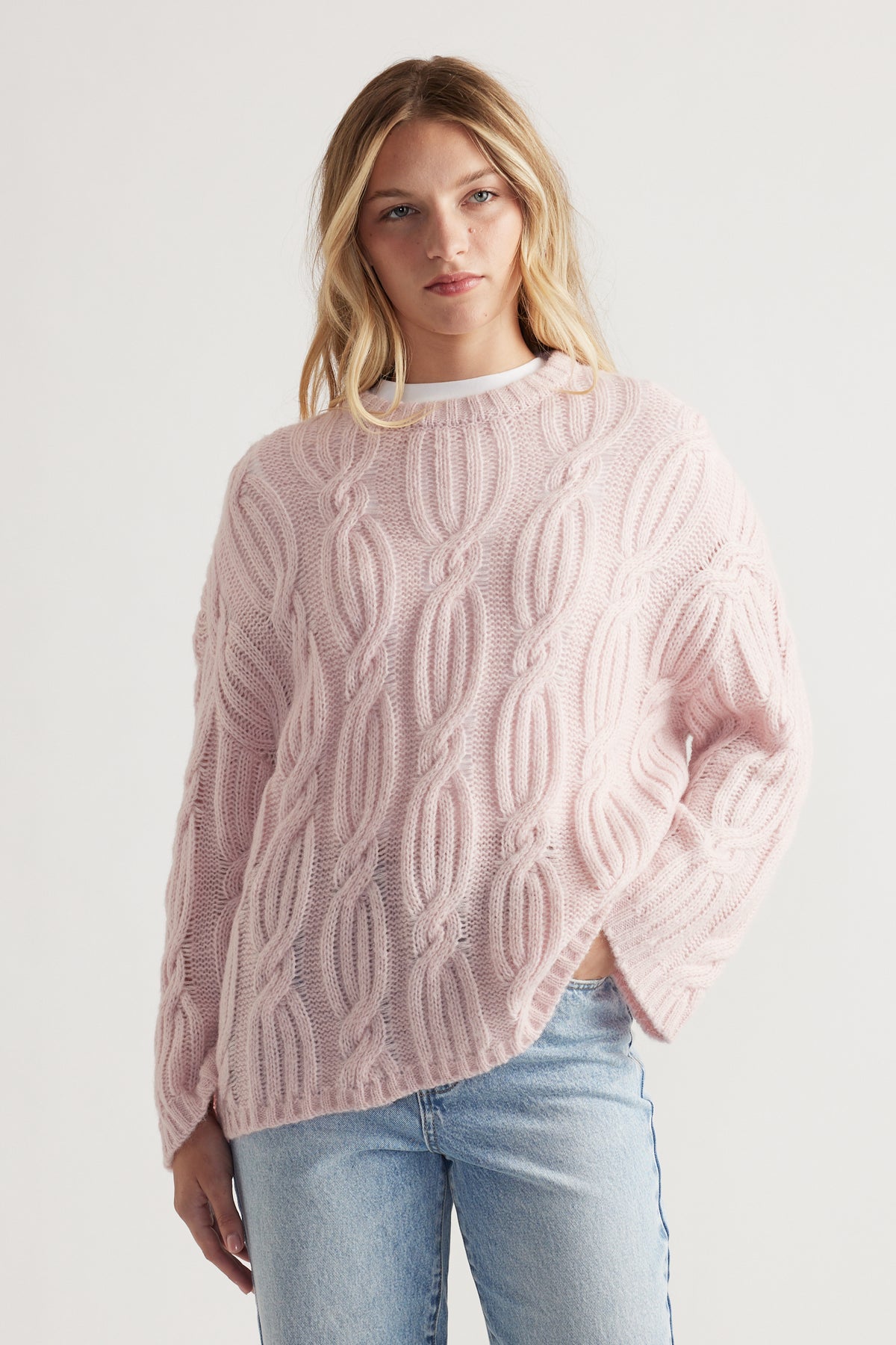 Woman wearing a soft pink cable knit jumper paired with light washed denim jeans in a relaxed style