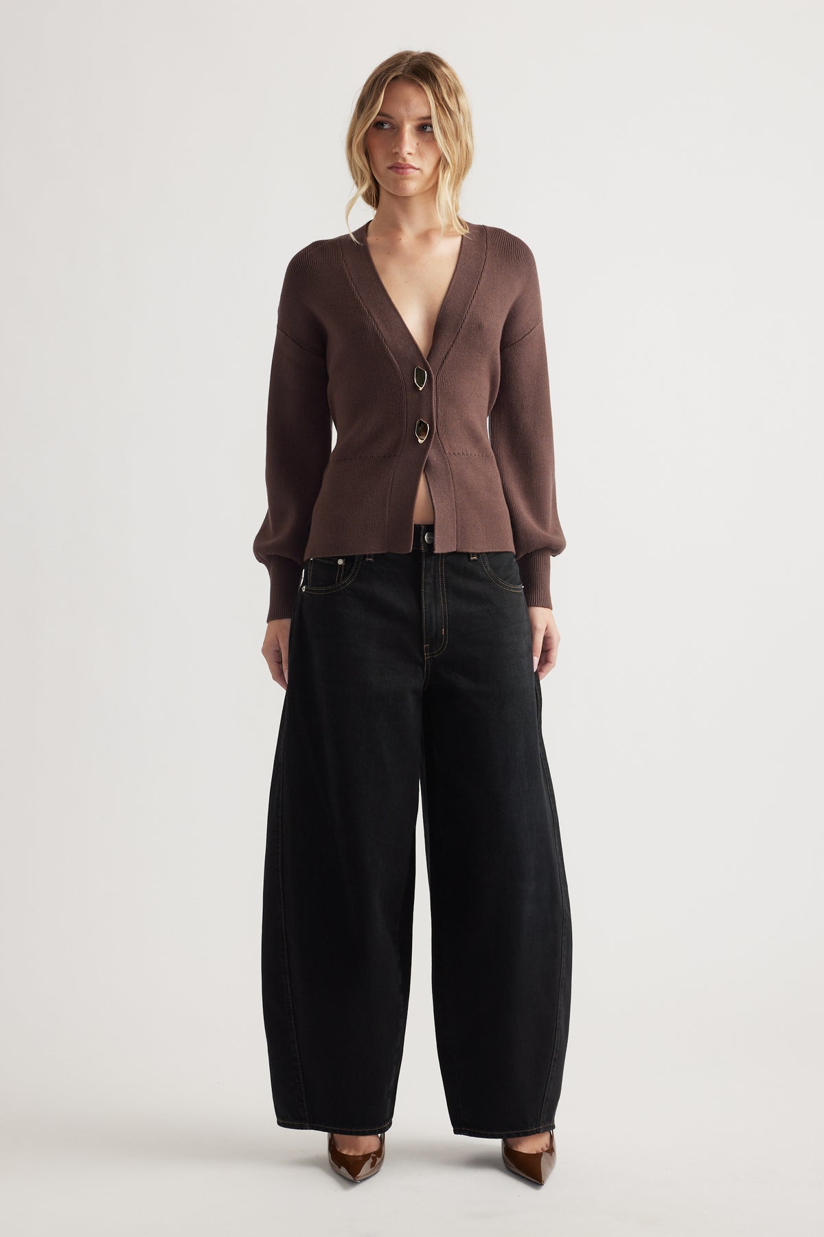 Woman wearing a brown knit cardigan with front closures paired with wide-leg black denim jeans and pointed heels