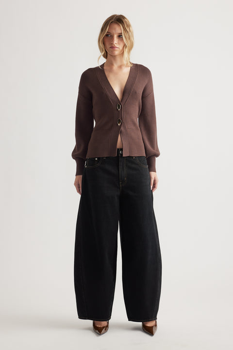 Woman wearing a brown knit cardigan with front closures paired with wide-leg black denim jeans and pointed heels