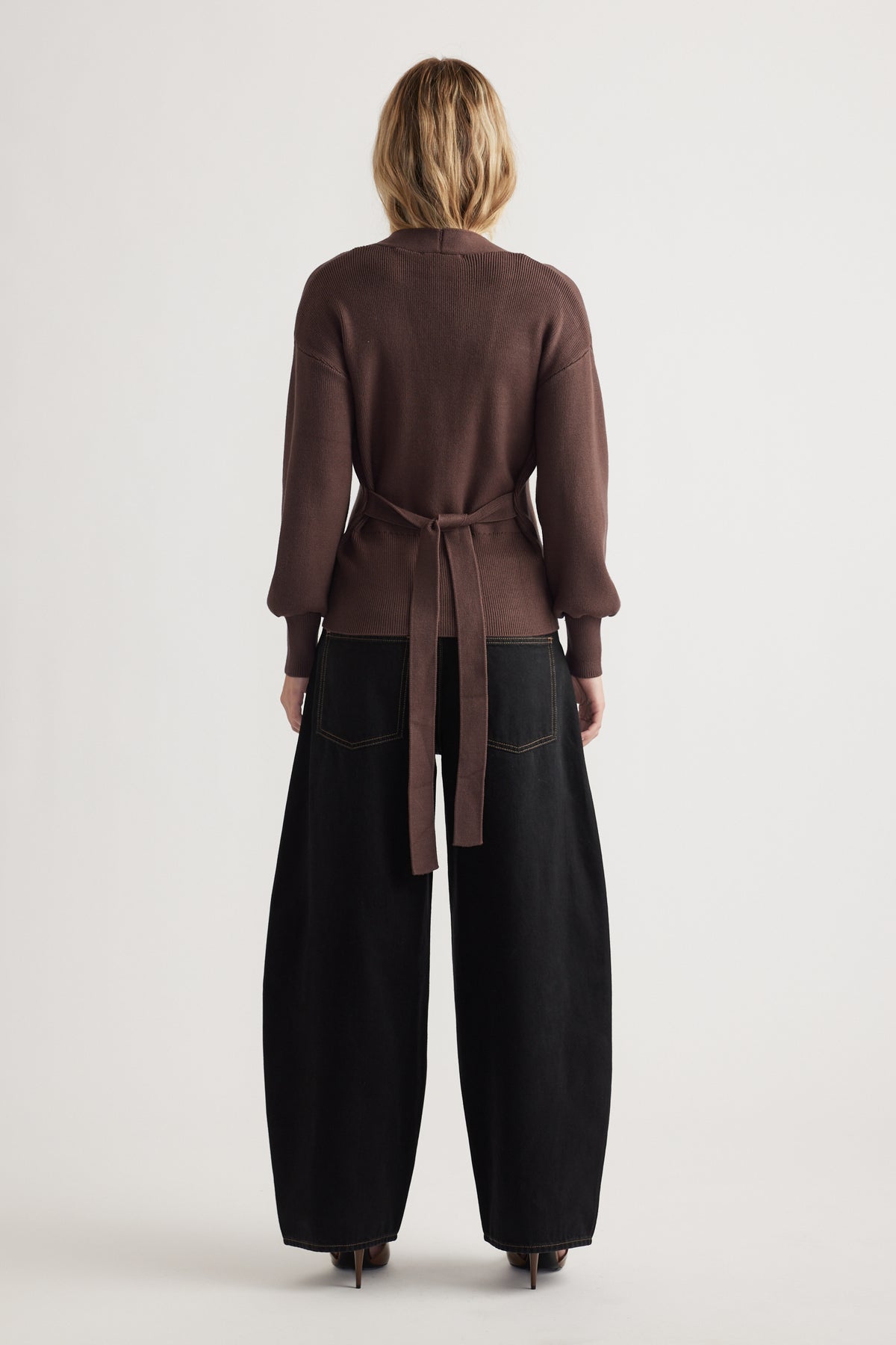 Back view of woman wearing a chocolate brown knit cardigan tied at the waist with loose black wide-leg pants and heels