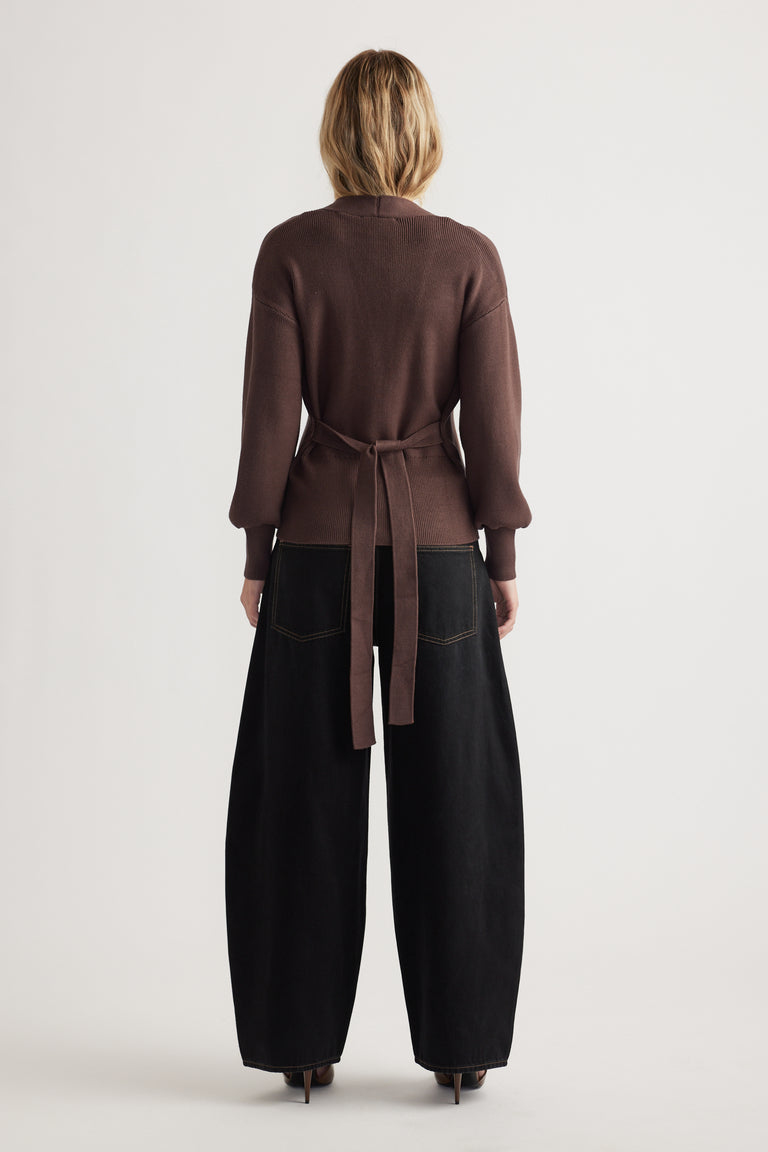 Back view of woman wearing a chocolate brown knit cardigan tied at the waist with loose black wide-leg pants and heels