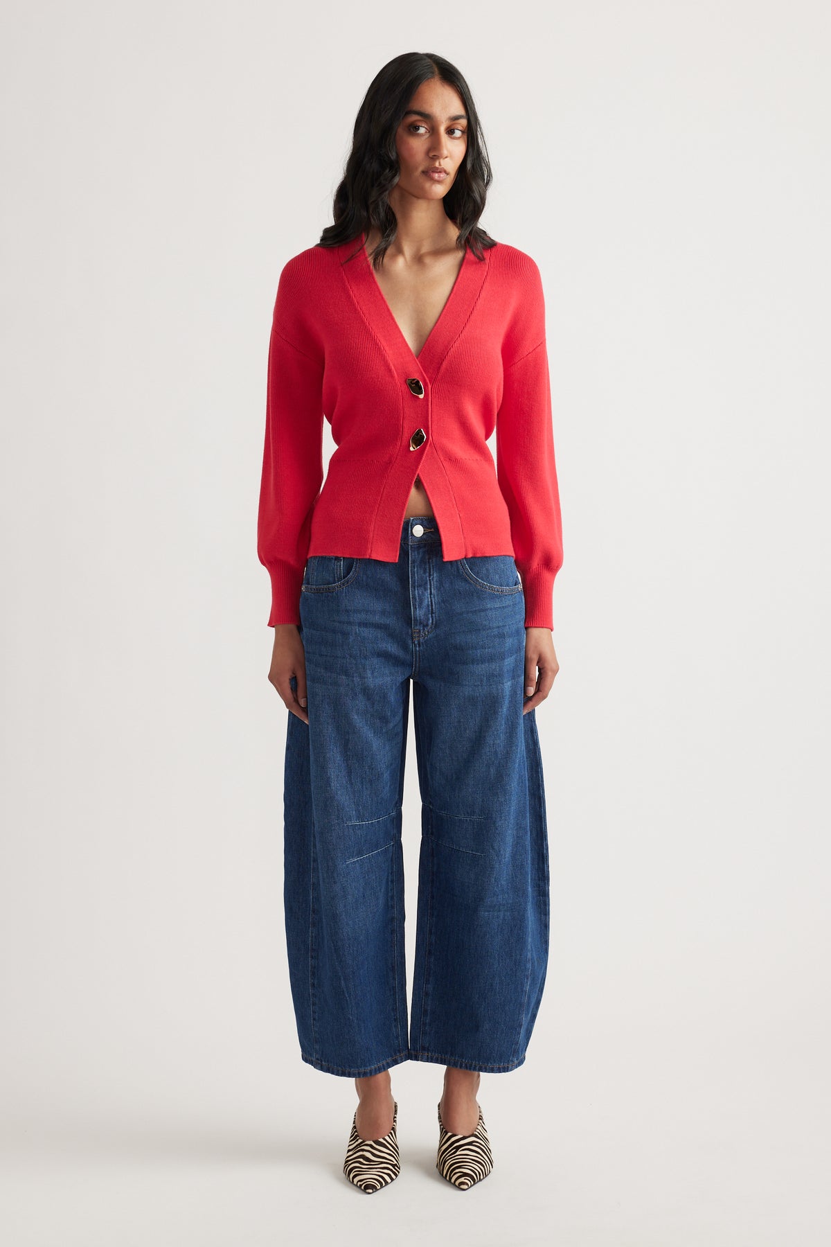 Woman wearing a vibrant red knit cardigan with large buttons paired with wide-leg cropped denim jeans and zebra print heels