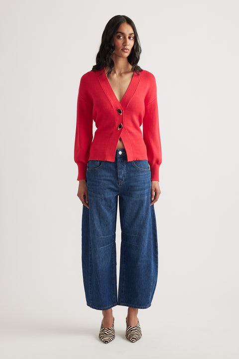 Woman wearing a vibrant red knit cardigan with large buttons paired with wide-leg cropped denim jeans and zebra print heels
