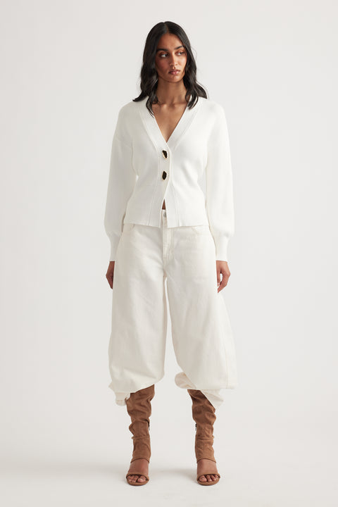 Woman wearing an ivory knit cardigan with tie-back detail paired with loose cream pants and tan ruched boots