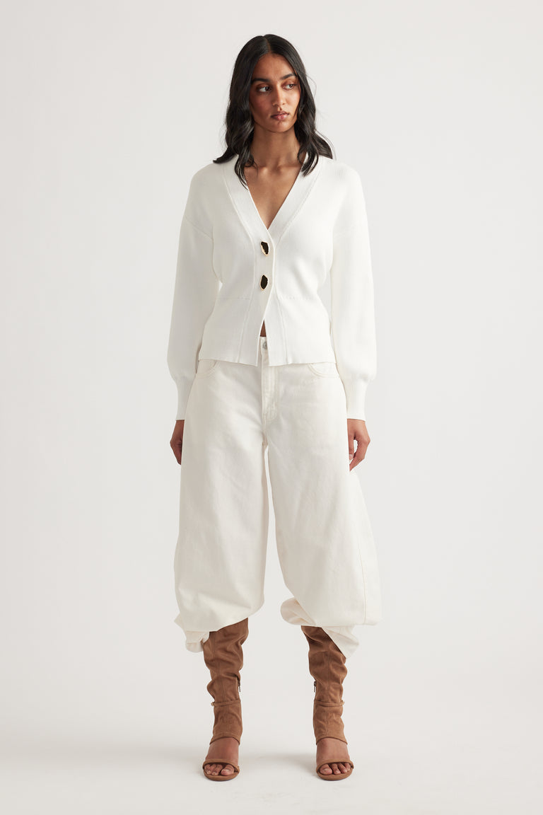 Woman wearing an ivory knit cardigan with tie-back detail paired with loose cream pants and tan ruched boots