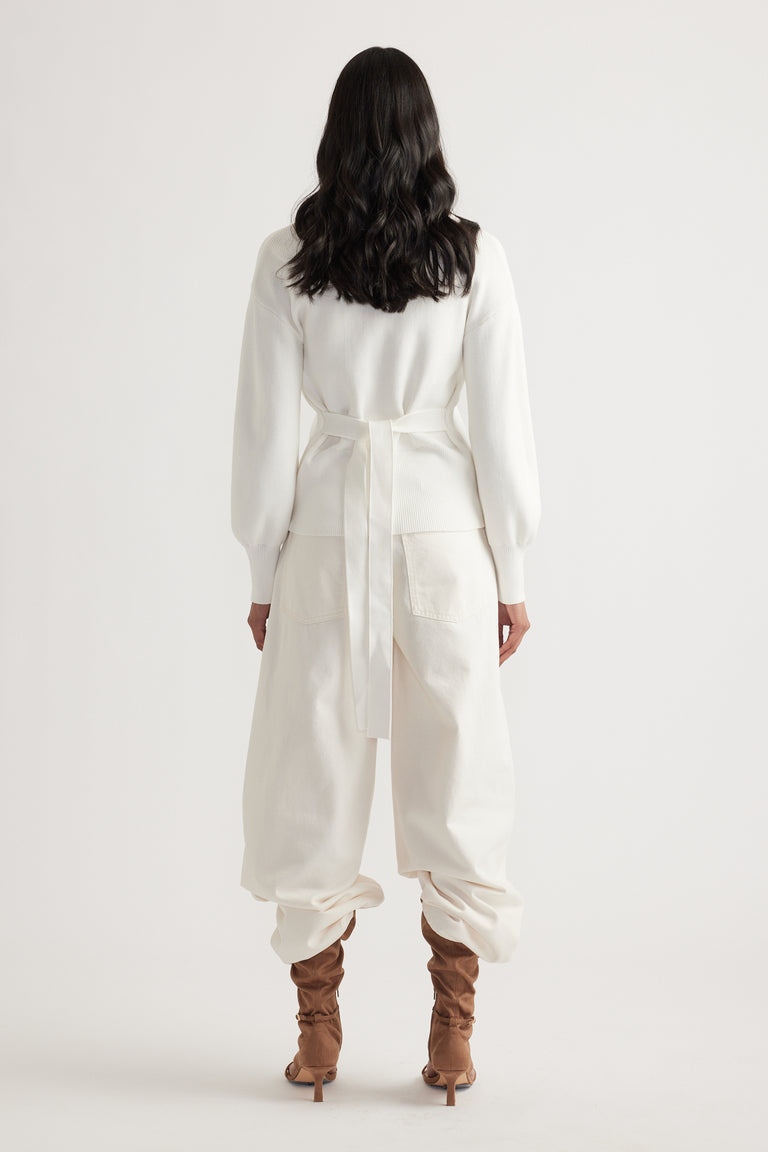 Woman seen from behind wearing an ivory knit cardigan with tie back detailing paired with loose cream pants and tan boots