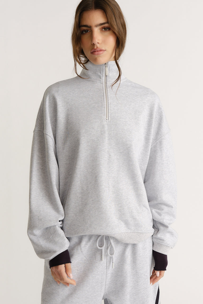 Woman wearing a soft light grey quarter-zip sweat with relaxed sleeves paired with matching drawstring pants for a cozy look