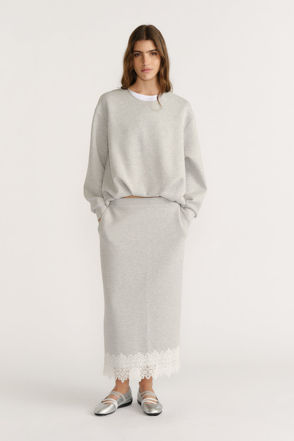 Woman in a soft grey midi skirt with lace trim paired with a relaxed sweatshirt and silver flats for an effortless look