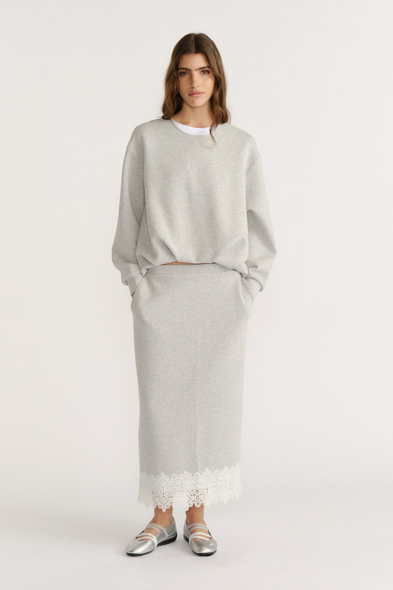 Woman in a soft grey midi skirt with lace trim paired with a relaxed sweatshirt and silver flats for an effortless look
