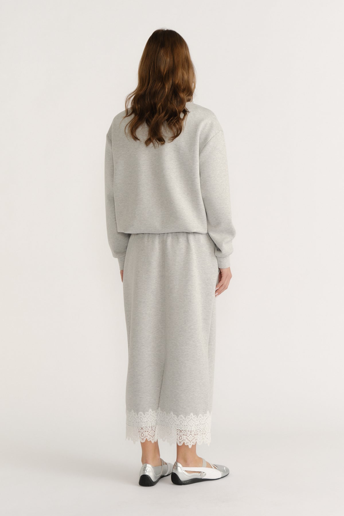 Woman wearing a soft grey midi skirt with lace trim paired with a matching relaxed sweatshirt and metallic flats