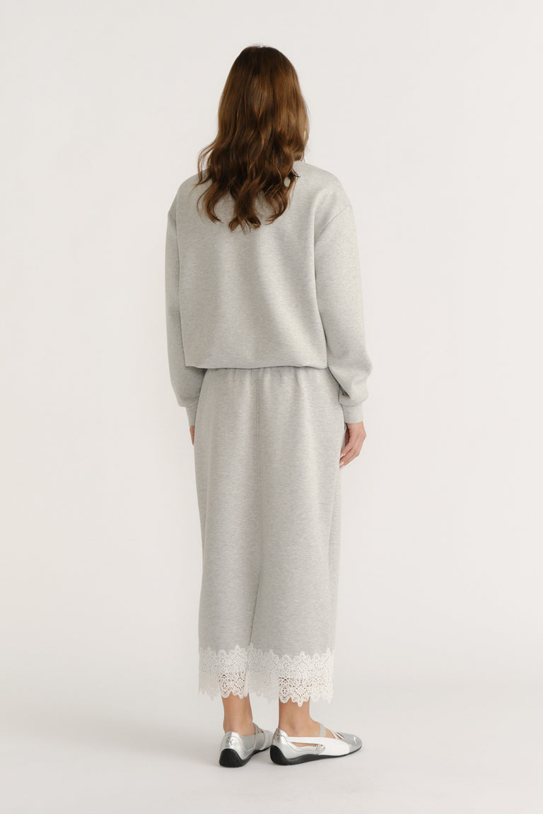 Woman wearing a soft grey midi skirt with lace trim paired with a matching relaxed sweatshirt and metallic flats