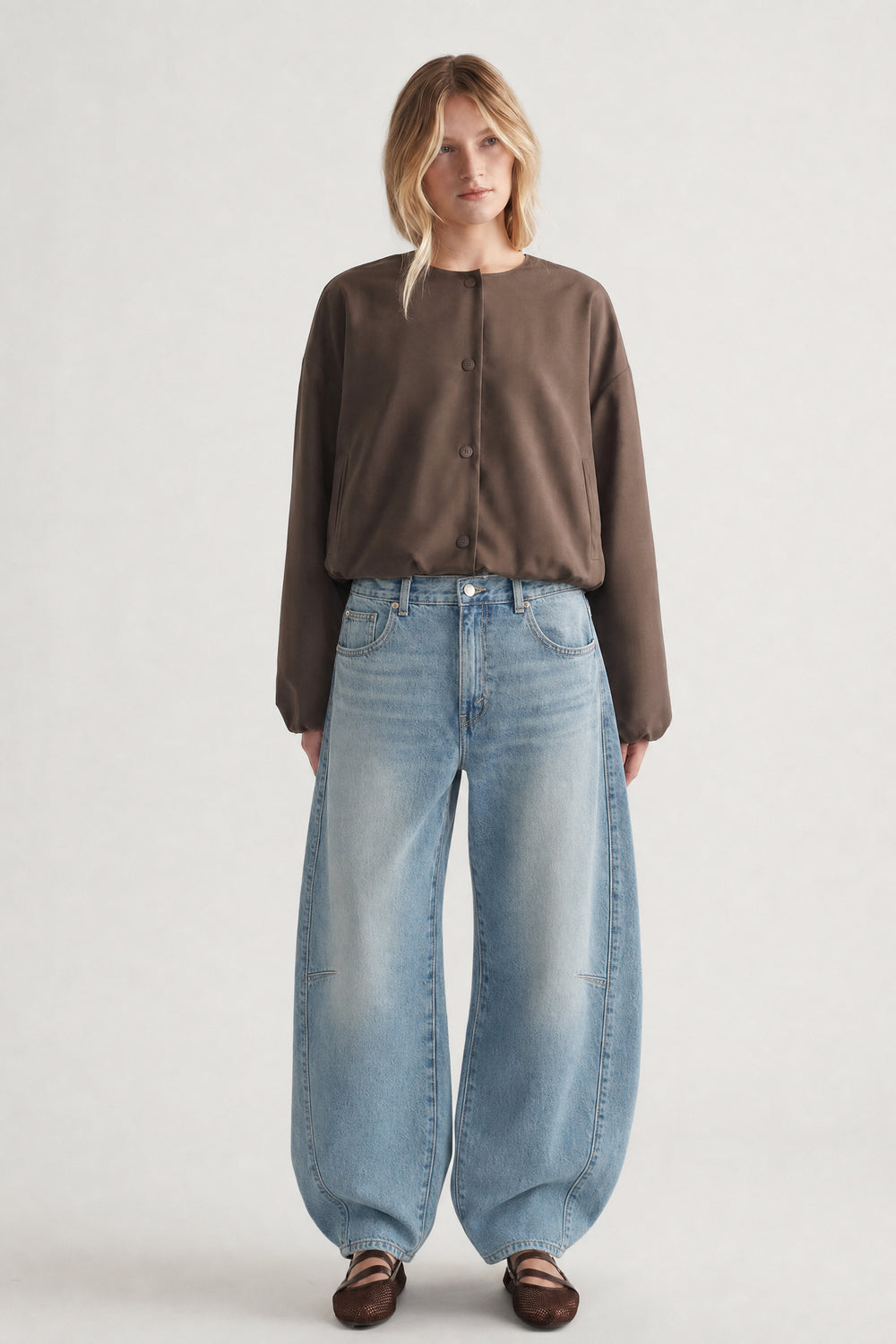 Front view of woman wearing a cropped brown button-up jacket with wide-leg light blue jeans and brown shoes