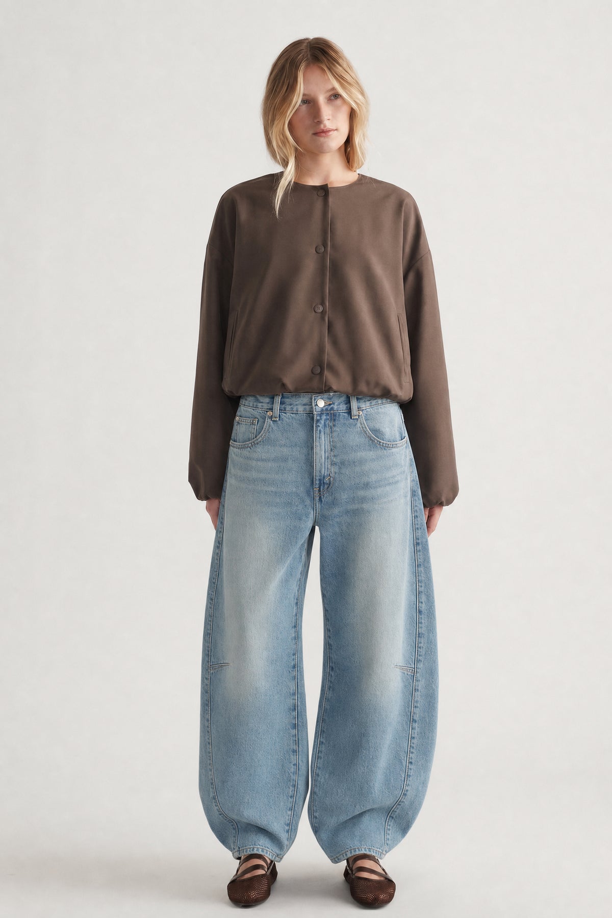 Front view of woman wearing a cropped brown button-up jacket with wide-leg light blue jeans and brown shoes
