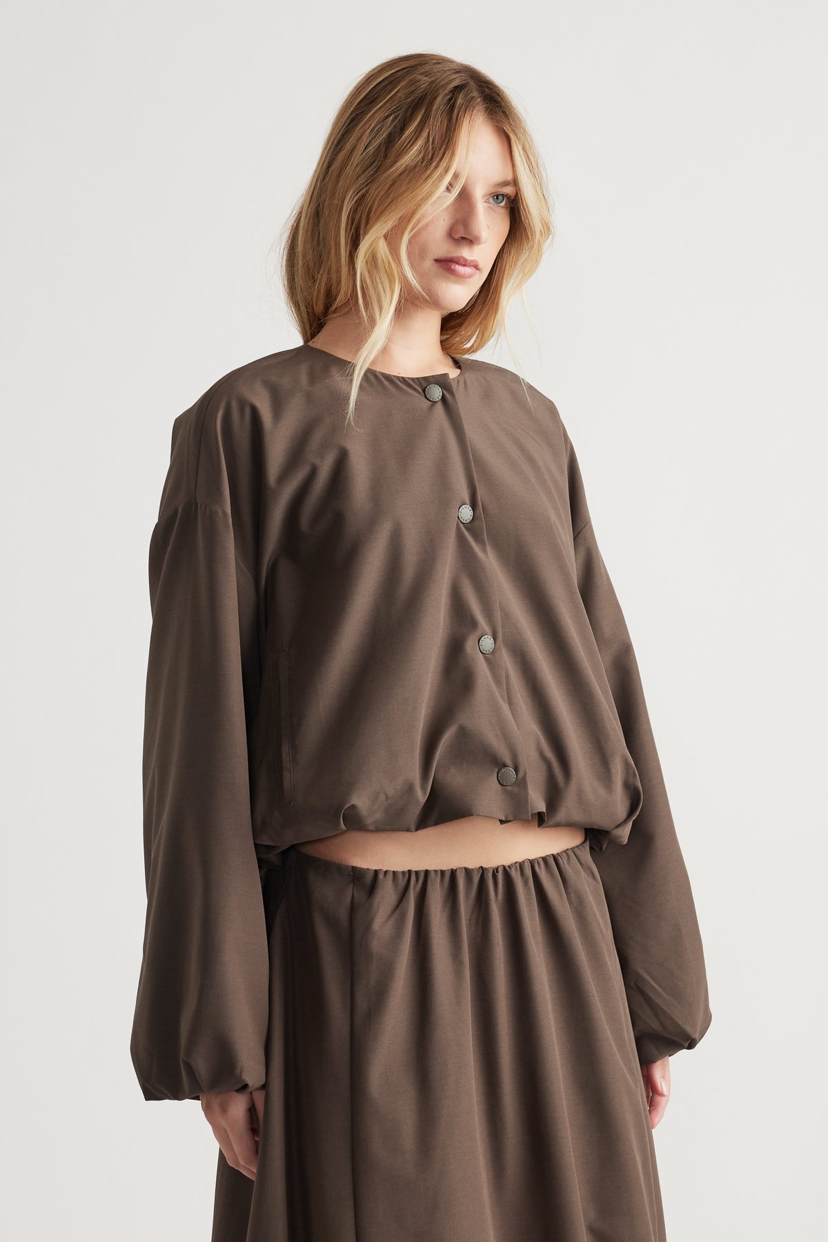 Woman wearing a relaxed-fit crop jacket with long balloon sleeves and button details in a warm brown tone