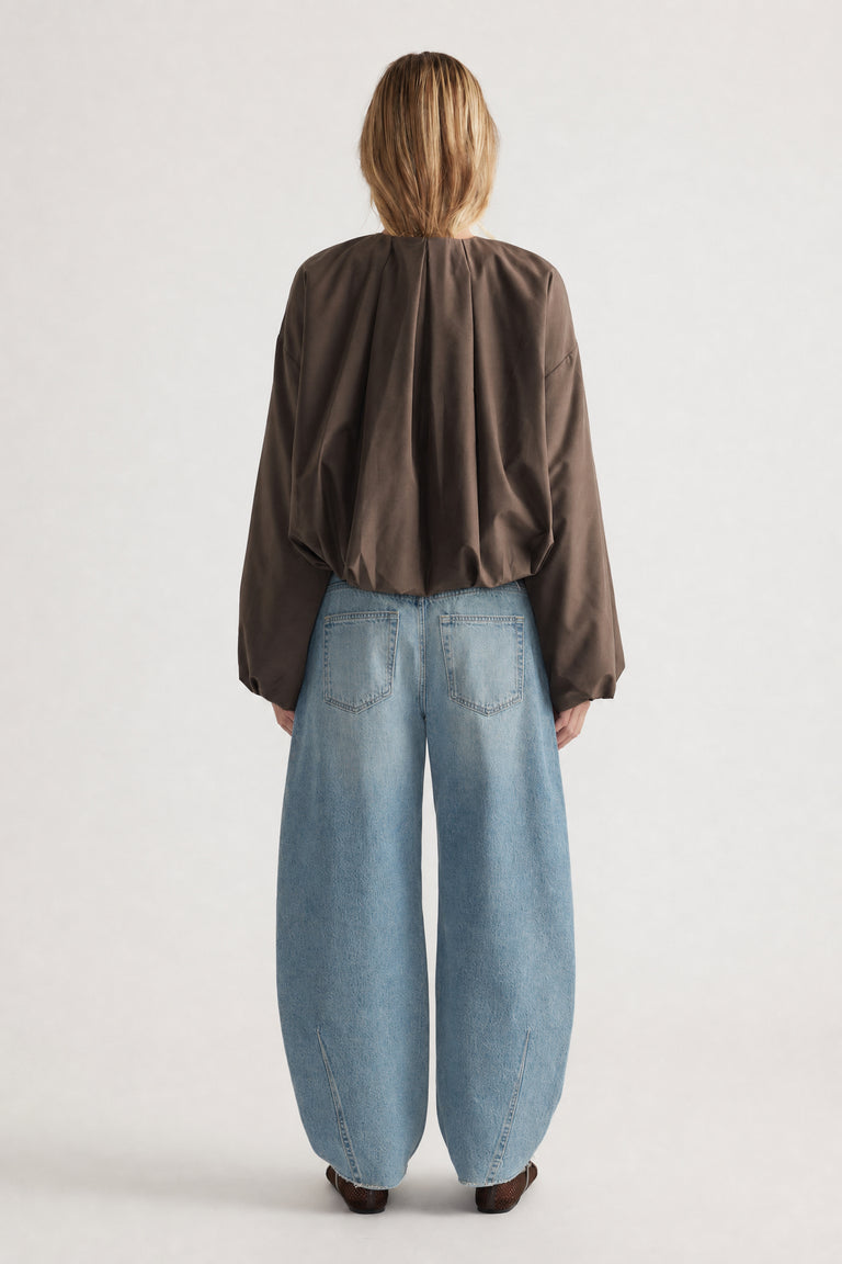 Rear view of woman wearing a cropped brown bubble jacket paired with loose, wide-leg light blue jeans and brown shoes