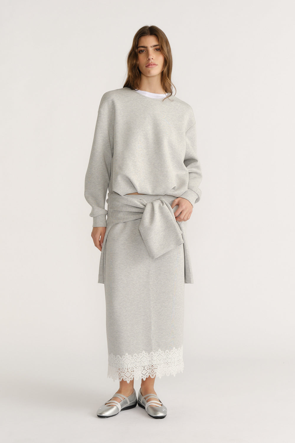 Woman wearing a soft grey sweat set with a tied sweatshirt detail and lace-trimmed midi skirt for a relaxed look