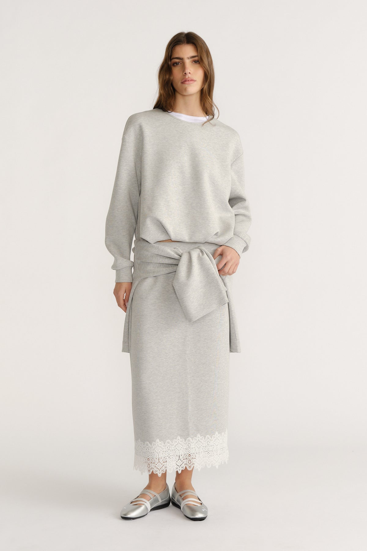 Woman wearing a soft grey sweat set with a tied sweatshirt detail and lace-trimmed midi skirt for a relaxed look