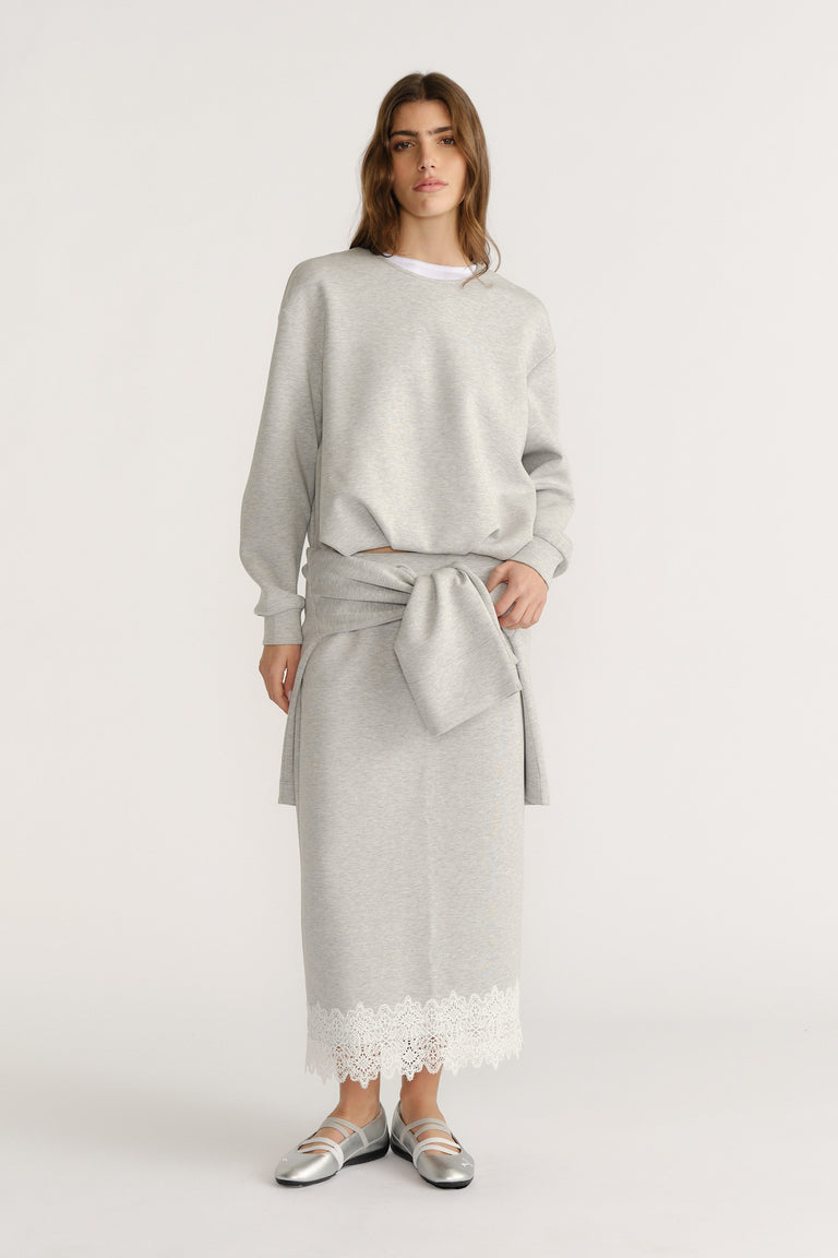 Woman wearing a soft grey sweat set with a tied sweatshirt detail and lace-trimmed midi skirt for a relaxed look