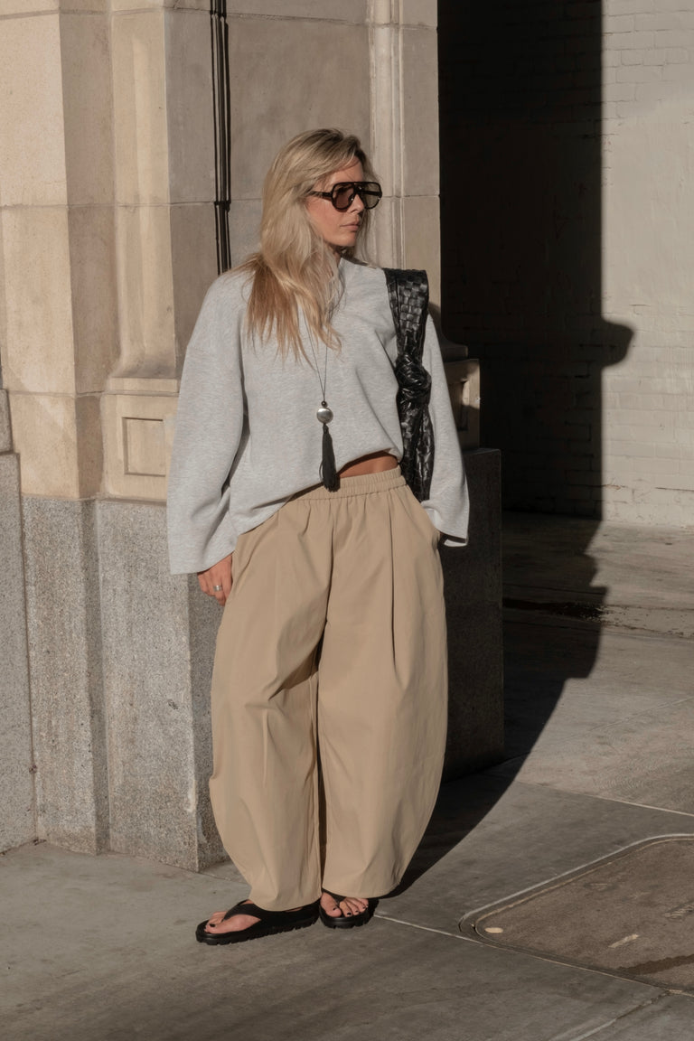 Woman wearing beige barrel-leg pants with a grey sweater, sunglasses and black sandals