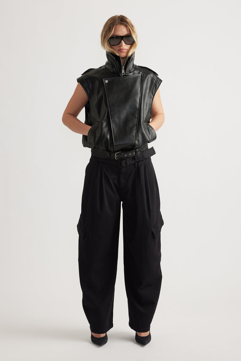 Woman styled in sleeveless black leather jacket with high collar and loose black balloon cargo pants with side pockets